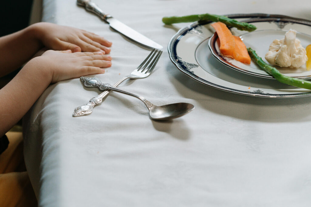 A child showing their hands on the dinner table, helping prepare the table for the meal.